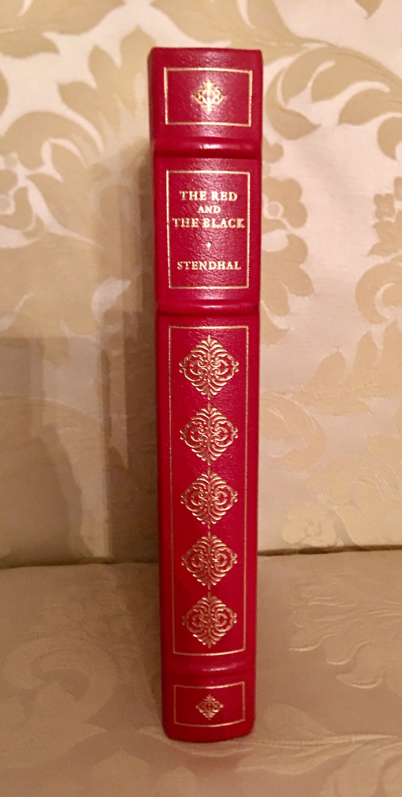 May include: A red hardcover book with gold lettering and decorative accents. The title is "The Red and the Black" by Stendhal.