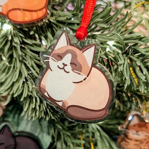 Può includere: Ornamenti natalizi a forma di gatto con finitura trasparente e glitterata. Gli ornamenti sono in vari colori, tra cui marrone, arancione e nero, e sono appesi a un albero di Natale verde. Ogni ornamento ha un nastro rosso per appenderli.