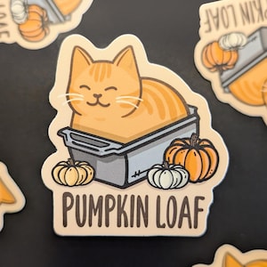 Op de afbeelding: Een sticker met een cartoon oranje kat in een broodvorm met een pompoenbrood en mini-pompoenen. De sticker zegt "Pumpkin Loaf" in wit lettertype.