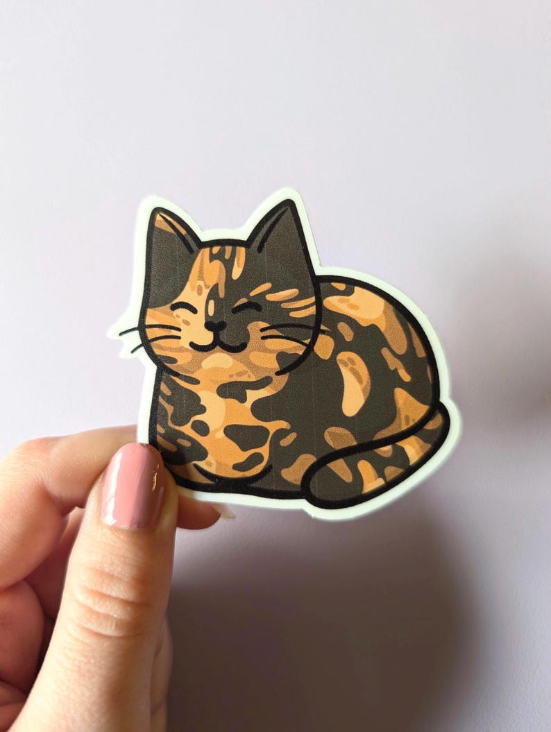 May include: A sticker of a cartoon calico cat with orange, black, and white fur. The cat is lying down and smiling.