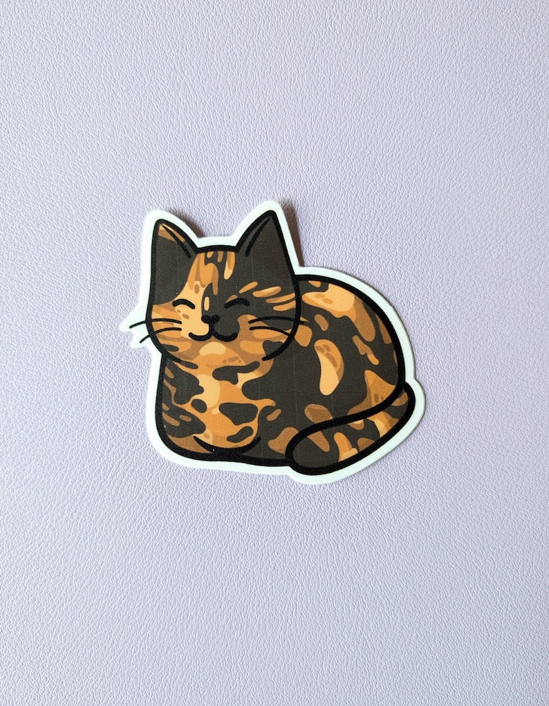 May include: A sticker of a cartoon cat with orange, black, and white fur. The cat is curled up and has a happy expression on its face.