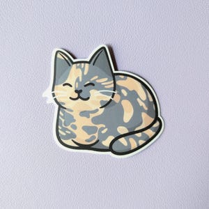 May include: A cartoon sticker of a calico cat with gray, orange, and white fur. The cat is curled up in a sleeping position with its eyes closed and a smile on its face.