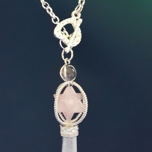 May include: A silver chain necklace with a clear crystal pendant. The pendant features a pink rose quartz star inside a silver cage.