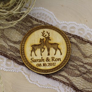 May include: A round wooden coaster with a laser-engraved design of two deer. The coaster has a brown wood grain and a dark brown border. The text "Sarah & Ron 08.10.2017" is engraved below the deer.