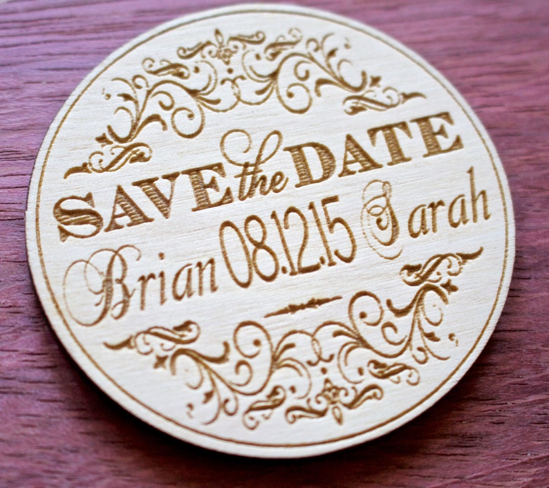 May include: Round wooden save the date magnet with a decorative floral design. The text reads "Save the Date Brian 08.12.15 & Sarah".