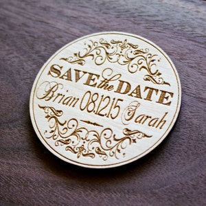 May include: Round wooden save the date sign with a decorative floral design. The sign reads "Save the Date" with the names "Brian & Sarah" and the date "08.12.15".