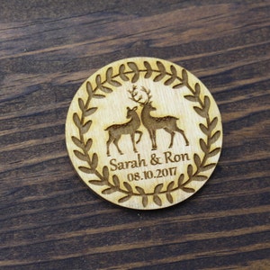 May include: Wooden round ornament featuring a wreath design and two deer silhouettes. The ornament is engraved with the text "Sarah & Ron 08.10.2017".