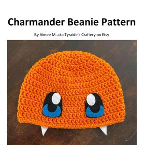 May include: Orange crochet beanie with white and blue felt eyes and white felt fangs. The beanie is on a brown wooden surface. Difficulty: Easy.