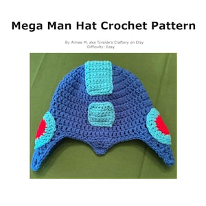 May include: A handmade blue crochet hat with turquoise and red accents, inspired by the Mega Man character. The hat features a unique design with ear flaps and a textured pattern. The text "Mega Man Hat Crochet Pattern" is visible.