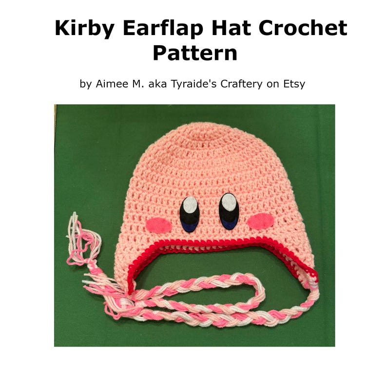 Pode incluir: Um chap&eacute;u rosa de croch&ecirc; com abas para as orelhas, acabamento vermelho e la&ccedil;os tran&ccedil;ados. O chap&eacute;u apresenta olhos bordados e bochechas rosa, que se assemelham a um personagem popular de videogame. O texto "Kirby Earflap Hat Crochet Pattern" est&aacute; no topo.