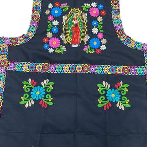 May include: Black apron with colorful floral embroidery and a central image of the Virgin of Guadalupe. The apron features a vibrant border of embroidered flowers and a pocket design with floral accents. A festive and decorative kitchen accessory.