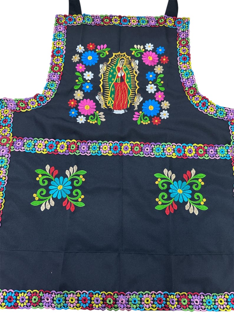 May include: Black apron with colorful floral embroidery and a central image of the Virgin of Guadalupe. The apron features a vibrant border of embroidered flowers and a pocket design with floral accents. A festive and decorative kitchen accessory.