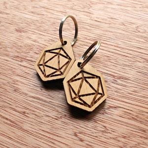May include: Two wooden keychains with geometric designs, each attached to a silver keyring. The keychains are light brown and feature a detailed, engraved pattern. The background is a wooden surface.