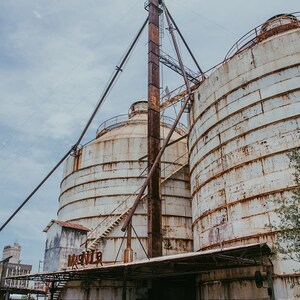 May include: Two large, white, metal silos with rusty accents. The silos are connected by a metal structure and have a ladder leading up to the top. The silos are surrounded by a metal frame and a metal roof. The word "Magnolia" is written on the side of one of the silos.