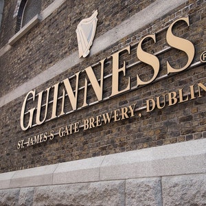 May include: A gold sign on a brick wall reads "GUINNESS" in large letters, followed by "ST. JAMES'S GATE BREWERY, DUBLIN" in smaller letters. The sign is on a building with a registered trademark symbol.