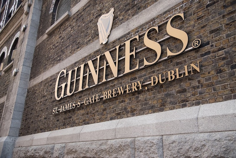 May include: A gold sign on a brick wall reads "GUINNESS" in large letters, followed by "ST. JAMES'S GATE BREWERY, DUBLIN" in smaller letters. The sign is on a building with a registered trademark symbol.