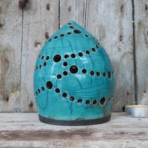 Op de afbeelding: Turquoise keramische kaarsenhouder met een geometrisch patroon van gaten. De houder heeft een afgeronde bovenkant en een platte basis.