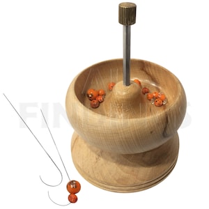 May include: A wooden bead spinner with a metal rod and a small bowl filled with orange beads. Two metal beading needles are included.