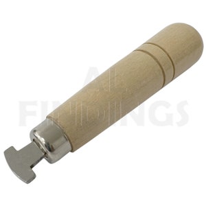 Puede incluir: Una herramienta con mango de madera y una cabeza de metal en forma de T. La herramienta se utiliza para colocar hallazgos de joyería.