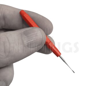 May include: A close-up of a hand holding a red and silver tool with a pointed tip. The tool is used for cleaning and maintaining electronic devices.