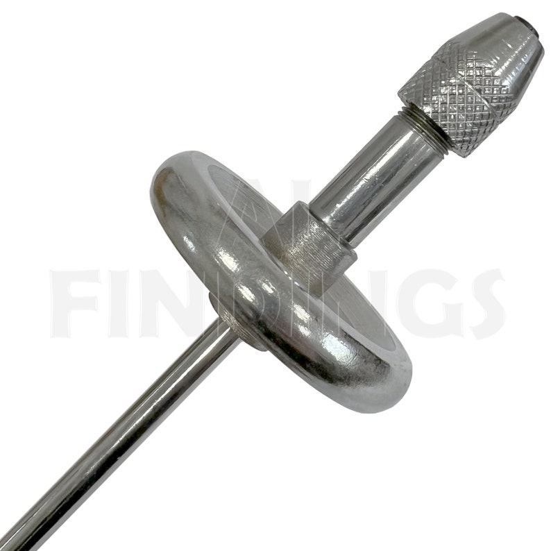 May include: A silver metal tool with a round base and a long, thin shaft. The shaft has a small, round, silver metal knob at the end. The tool is used for drilling or turning.