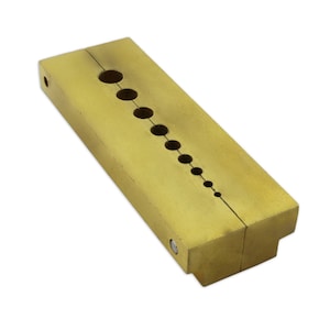 May include: A rectangular brass tool with a series of graduated holes. The tool is split in two halves and has a small rectangular extension on one end. The holes are arranged in a diagonal line.