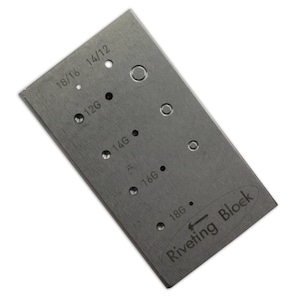 Puede incluir: Un bloque de remachado de metal plateado con una variedad de agujeros de diferentes tamaños para remaches de diferentes calibres. El bloque está etiquetado como "Riveting Block" e incluye los tamaños 18/16, 14/12, 12G, 14G, 16G y 18G.