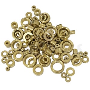 May include: A selection of brass hardware components, including washers, bushings, and cylindrical pieces. The components are in various sizes and shapes, with a shiny, golden finish. The items are scattered across a white background.