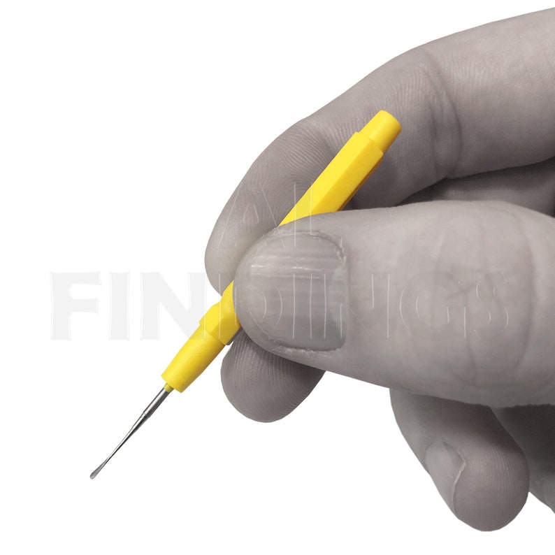 May include: A yellow plastic tool with a thin, pointed metal tip. The tool is held in a gloved hand.