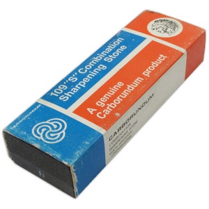 May include: A blue and red box with the text "109"S" Combination Sharpening Stone" and "A genuine Carborundum product". The box contains a black sharpening stone.