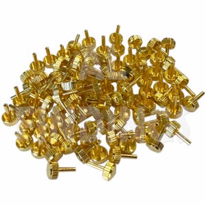 Peut inclure: Un tas de petits composants métalliques dorés. Chaque pièce a une base ronde, un corps cylindrique strié et une petite broche saillante. Les composants sont dispersés sur un fond blanc, la lumière se reflétant sur leurs surfaces brillantes.
