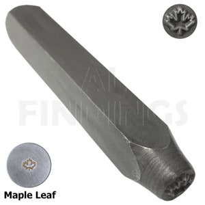 Puede incluir: Un punzón de metal con un diseño de hoja de arce. El punzón es de color plateado y tiene una forma hexagonal. El punzón se utiliza para crear impresiones en metal.