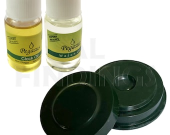 May include: Two small bottles of clear oil with white caps. The bottles are labeled "Pegasus Clock Oil" and "Pegasus Watch Oil". The bottles are next to two green round objects.