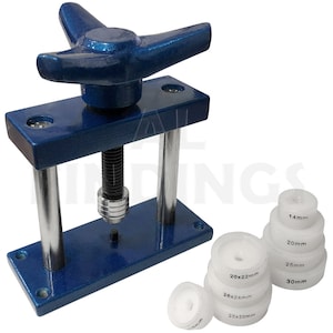 Könnte beinhalten: Eine blaue Metall-Uhrenpresse mit Handkurbel und einem Satz weißer Kunststoff-Uhrengehäusepressmatrizen. Die Matrizen sind mit Größen in Millimetern beschriftet: 14 mm, 20 mm, 25 mm, 30 mm, 20 x 22 mm, 26 x 24 mm, 28 x 30 mm.