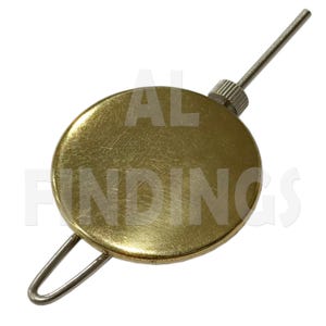 May include: A circular gold-toned metal clock pendulum bob featuring a smooth, reflective surface. It includes a threaded silver-toned adjustment nut at the top with a thin metal rod extending upwards and a wire loop attached to the bottom edge.