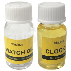 May include: Two small bottles of oil with yellow labels. The bottle on the left is labeled "alfindings WATCH OIL Non Cloggy Non Drying". The bottle on the right is labeled "alfindings CLOCK OIL Non Cloggy Non Drying".