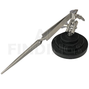 May include: A silver-toned, adjustable, third hand tool with a pair of tweezers and a weighted base. The base is black and has a textured surface.