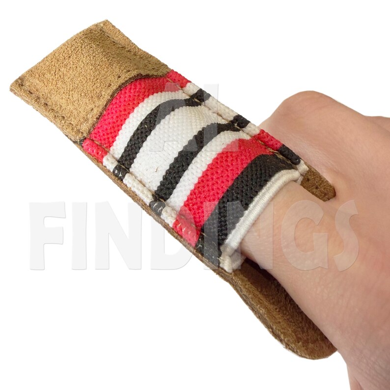 May include: A finger protector with a tan leather exterior and a striped pattern in red, black, and white. The protector is designed to fit over a finger, likely for archery or similar activities.