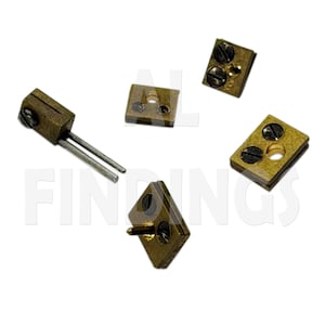 May include: A collection of four small brass-toned metal components, each featuring a rectangular base with two dark screws. One piece includes two long, thin silver-toned metal pins extending from the side, while another has a single small pin.