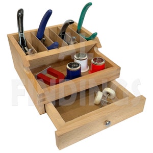 Peut inclure: Une boîte en bois avec un tiroir, contenant divers outils et fournitures. La partie supérieure comporte un compartiment pour ranger les outils, et le tiroir inférieur comporte un petit compartiment pour ranger d'autres articles. Les outils comprennent des pinces, des pincettes et une loupe. Les fournitures comprennent un aimant, une bobine de fil et un petit morceau de feutre.