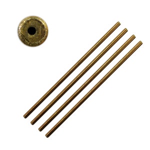 Pode incluir: Quatro hastes de metal de cor dourada, cada uma com um comprimento ligeiramente diferente, estão dispostas em diagonal. Um único disco de metal dourado com um furo no centro é mostrado no canto superior esquerdo da imagem.