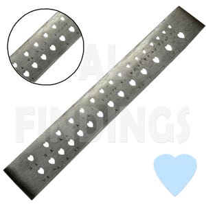 Puede incluir: Una regla de metal plateada con agujeros en forma de corazón. La regla está marcada con números del 1 al 30. La regla mide aproximadamente 30 cm de largo.