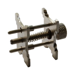 May include: A silver watch band spring bar tool with a threaded knob and two spring-loaded pins.