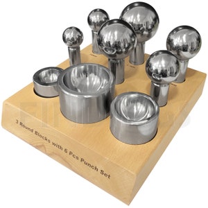 Puede incluir: Un juego de herramientas para dar forma a metales, que incluye seis punzones esféricos y tres bloques redondos, exhibidos sobre una base de madera. El texto en la base dice "3 Round Blocks with 6 Pcs Punch Set". Los punzones varían en tamaño.