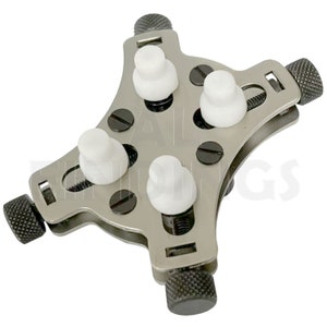 May include: A silver watch case holder with four white adjustable knobs and three black knobs. The holder is designed to hold a watch securely while working on it.