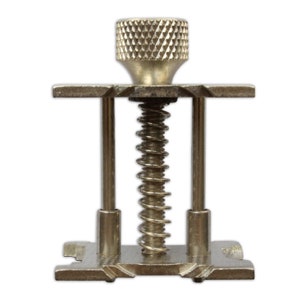 May include: A silver metal clamp with a spring and a knob on top. The clamp is used for holding objects together.