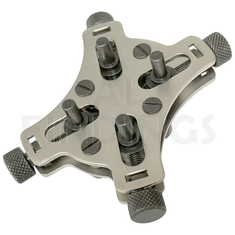 May include: A silver watch case holder with four adjustable arms. Each arm has a knurled knob and a threaded post. The holder is designed to securely hold a watch case while working on it.