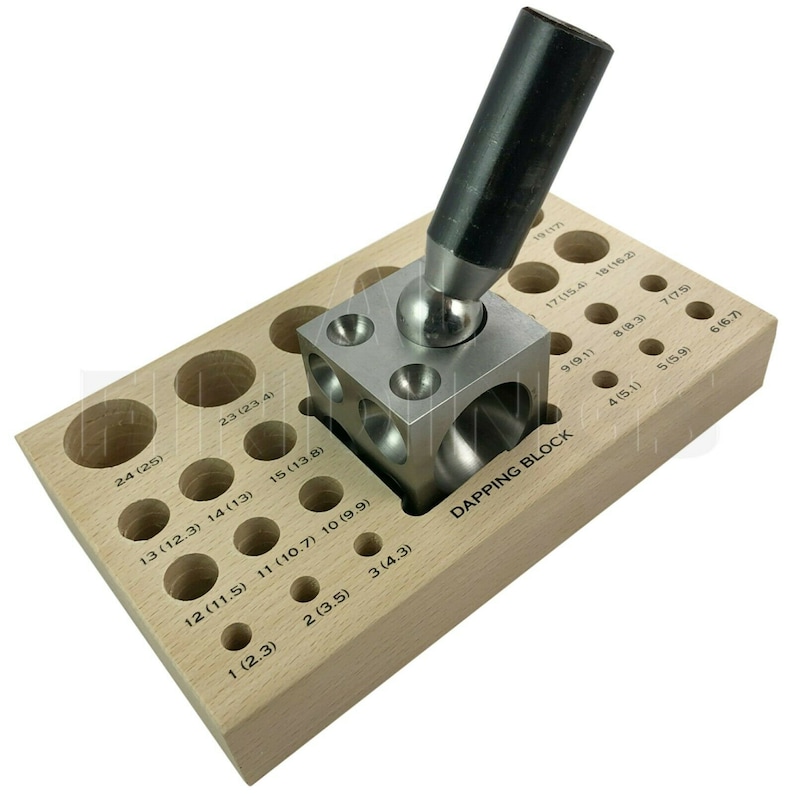 Op de afbeelding: Een houten dappingblok met verschillende gaten voor het vormen van metaal. Het blok heeft een metalen dappingtool met een bolvormige kop die in een van de gaten rust.