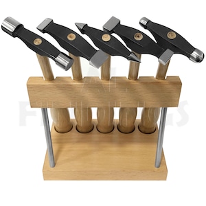 Puede incluir: Conjunto de seis martillos de metal con mangos de madera, expuestos en un soporte de madera. Los martillos tienen cabezas de diferentes formas, incluyendo redondas, cuadradas y puntiagudas.