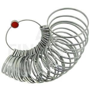 Puede incluir: Un medidor de talla de anillos de plata con un punto rojo en el mango. El medidor está formado por una serie de anillos graduados que se pueden utilizar para determinar el tamaño de un anillo.